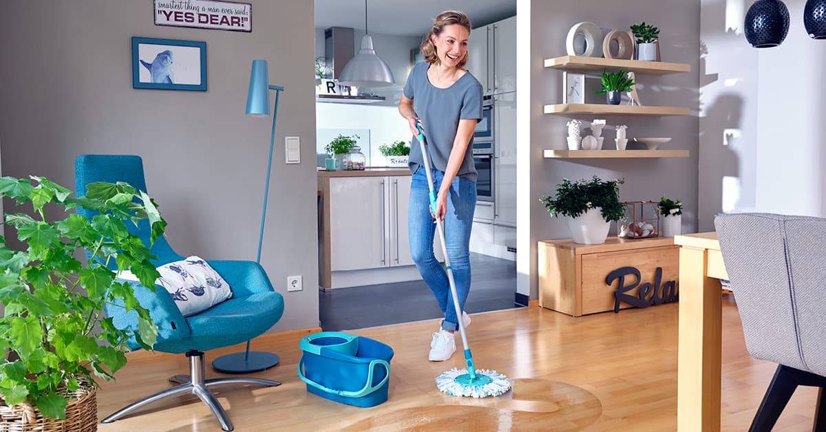 Woman moping a living room with blue bucket next to her