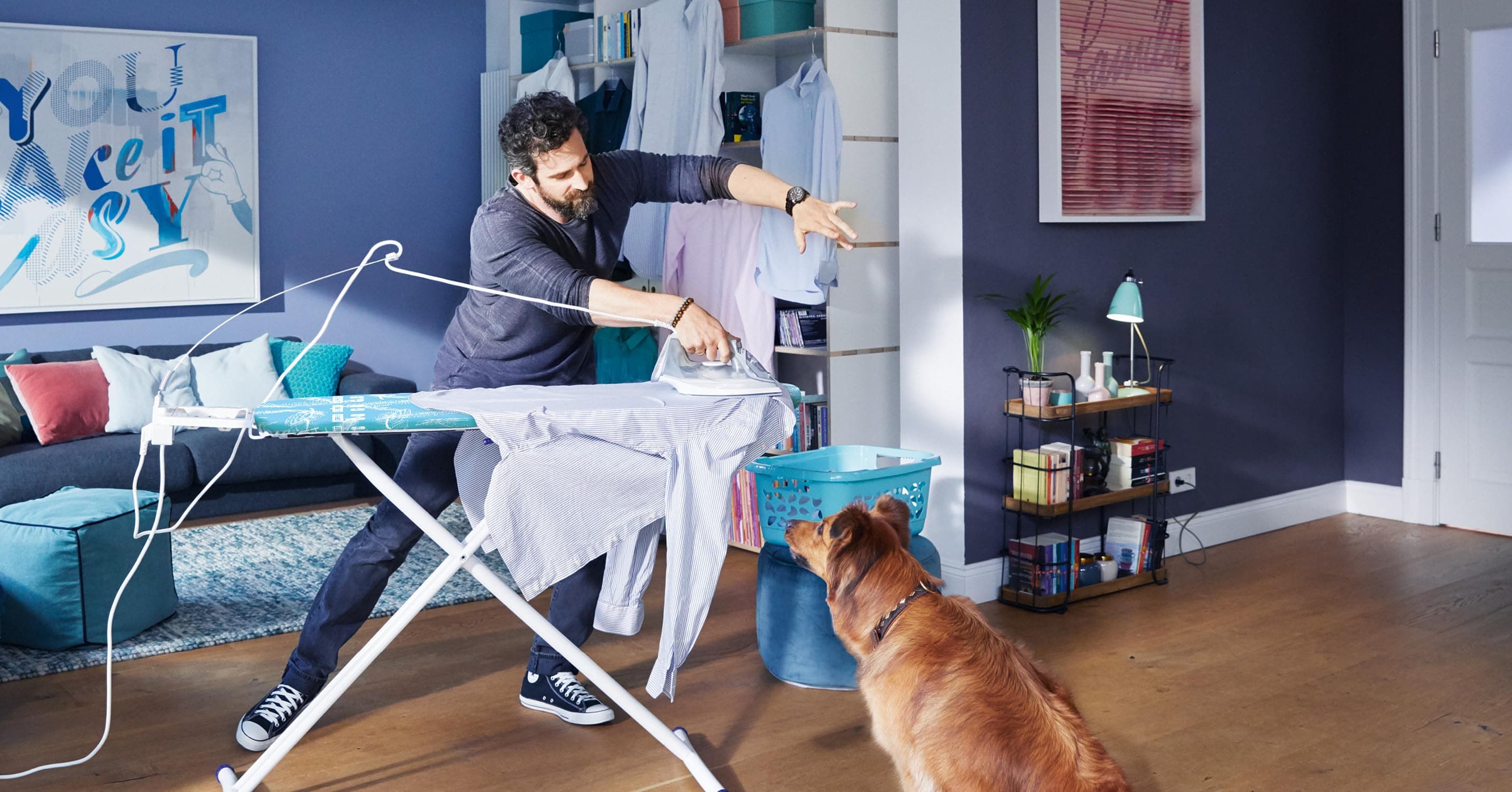 Man ironing with a dog looking at him